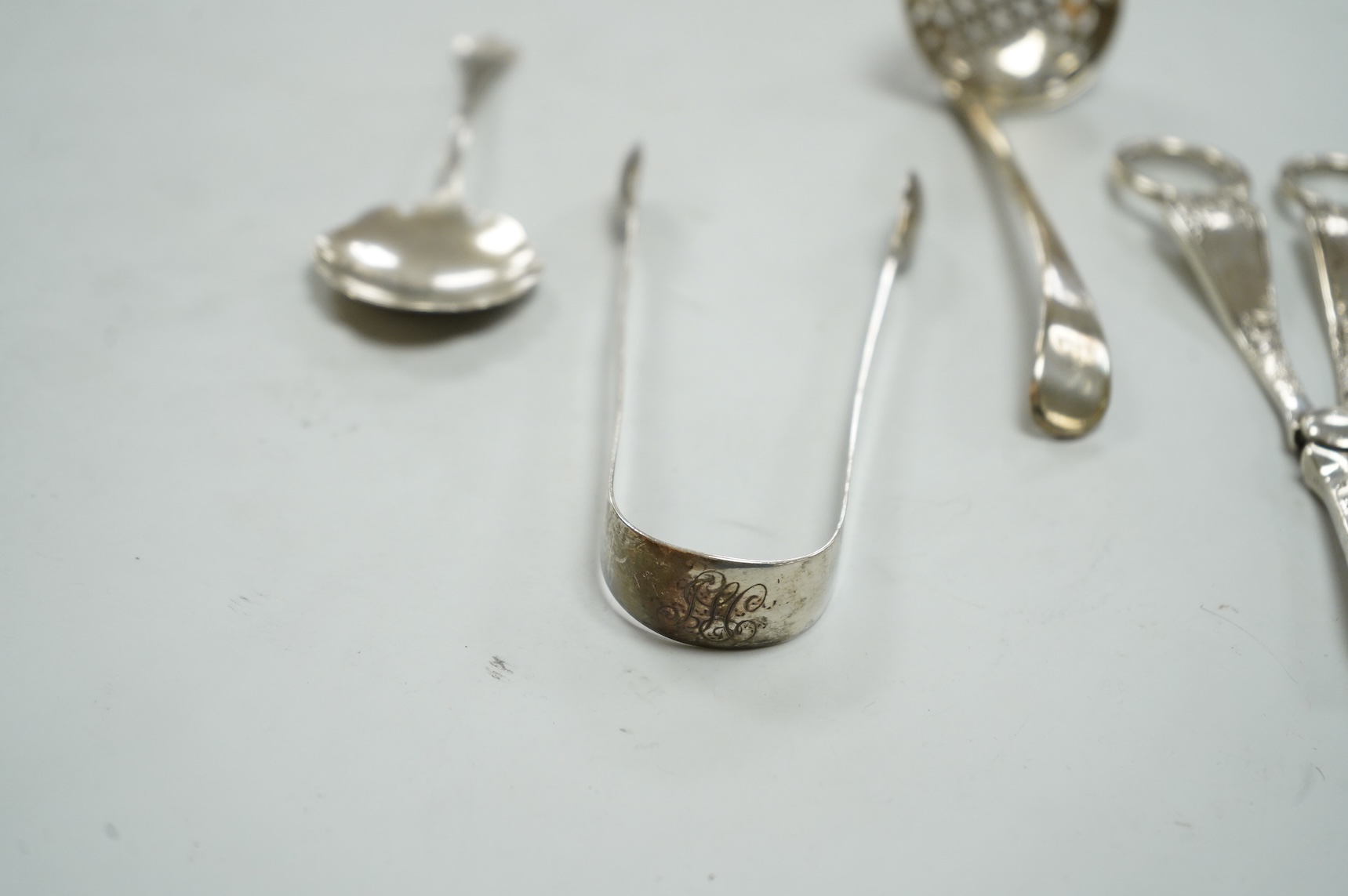 A pair of George V silver grape shears, Josiah Williams & Co, London, 1912, 16.2cm, together with a George III silver Old English pattern sifter spoon, Eley & Fearn, London, 1801, a similar pair of sugar tongs, London, 1